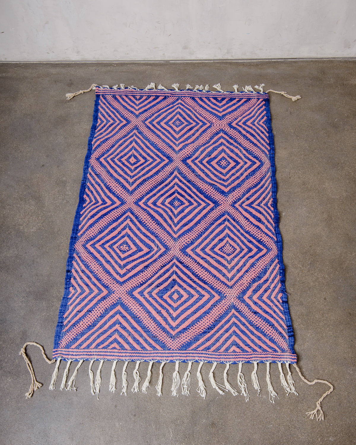 Small Berberlin Kelim Rug in pink and blue laying on concrete floor.